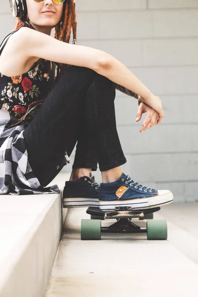 Young girl with tattoo and dreadlocks listening to music while sitting on the steps — Stock Photo, Image