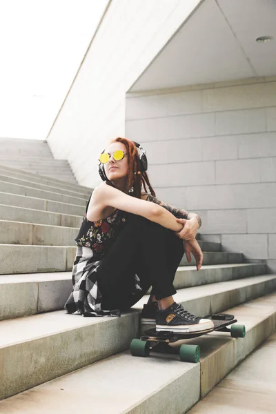 Молода дівчина з татуюванням і дредлоками слухає музику, сидячи на сходах — стокове фото