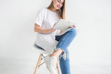 Beyaz bir T-shirt ve kot tablet beyaz bir arka plan üzerinde kullanma genç şık sarışın kız portresi
