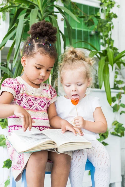 Dua gadis kecil membaca buku tentang latar belakang tanaman dalam pot — Stok Foto