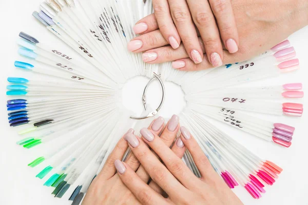 Top view of beautiful womans hands with collection of color nail polish samples on white background