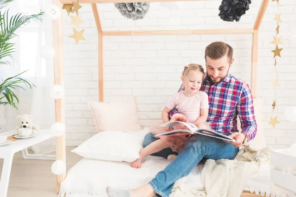 Dad and daughter sit together and read a book.