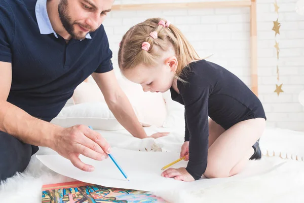 Un joven padre y su hija yacen en el suelo y dibujan con lápices de colores . — Foto de Stock