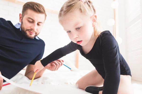 Un joven padre y su hija yacen en el suelo y dibujan con lápices de colores . — Foto de Stock