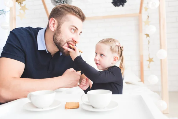 Linda niña y su padre beben té con galletas en casa . — Foto de Stock