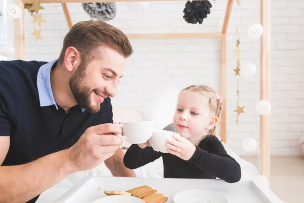 Linda niña y su padre beben té con galletas en casa . — Foto de Stock
