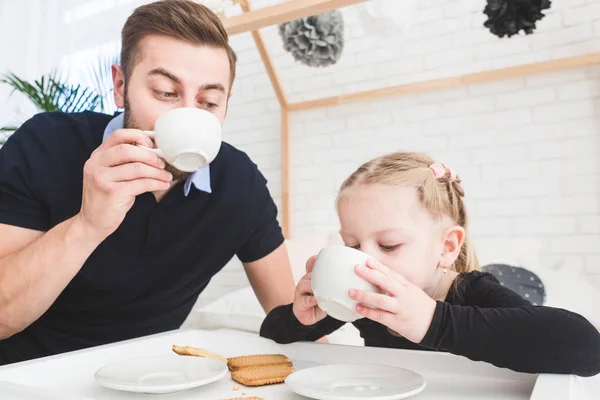 Linda niña y su padre beben té con galletas en casa . — Foto de Stock