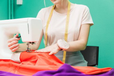 Dikiş atölyesi. Terzi iş başında. Dikiş makinesi ile renkli bir arka plan üzerine çalışan genç kadın