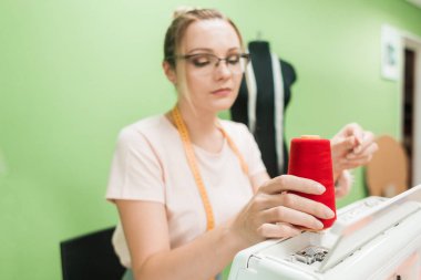 Dikiş atölyesi. Terzi iş başında. Dikiş makinesi ile renkli bir arka plan üzerine çalışan genç kadın