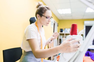 Dikiş atölyesi. Terzi iş başında. Dikiş makinesi ile renkli bir arka plan üzerine çalışan genç kadın