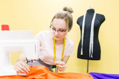 Dikiş atölyesi. Terzi iş başında. Dikiş makinesi ile renkli bir arka plan üzerine çalışan genç kadın