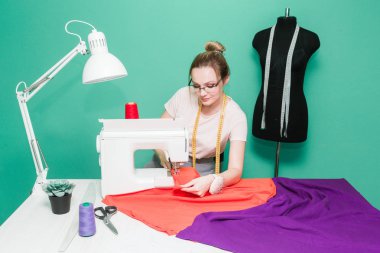 Dikiş atölyesi. Terzi iş başında. Dikiş makinesi ile renkli bir arka plan üzerine çalışan genç kadın