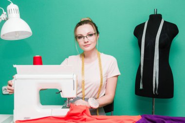 Dikiş atölyesi. Terzi iş başında. Dikiş makinesi ile renkli bir arka plan üzerine çalışan genç kadın