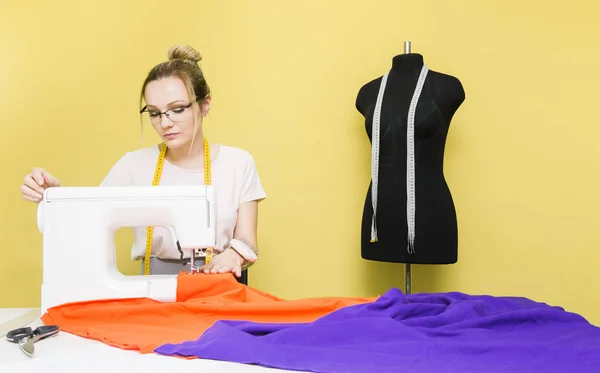 Nähwerkstatt. Näherin bei der Arbeit. junge Frau arbeitet mit Nähmaschine auf farbigem Hintergrund — Stockfoto