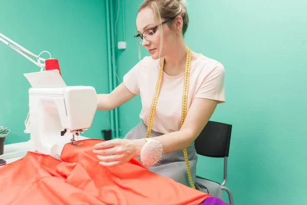 Nähwerkstatt. Näherin bei der Arbeit. junge Frau arbeitet mit Nähmaschine auf farbigem Hintergrund — Stockfoto