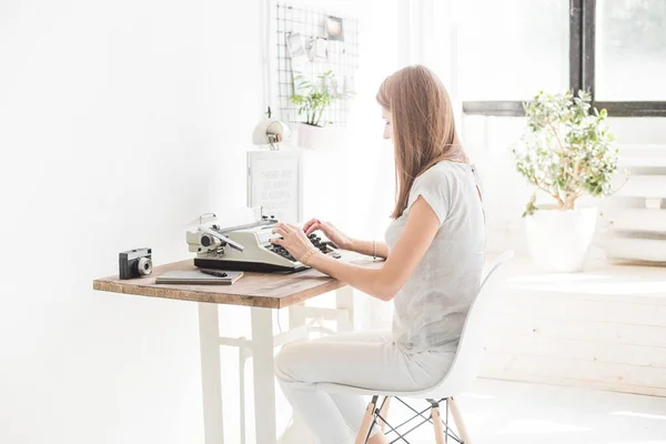 Νεαρή γυναίκα εργάζεται στο σπίτι και πληκτρολογώντας σε μια γραφομηχανή. Δημιουργική σκανδιναβικό στυλ χώρου εργασίας — Φωτογραφία Αρχείου
