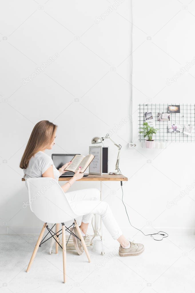 Young business woman working at home and reading a book. Creative Scandinavian style workspace