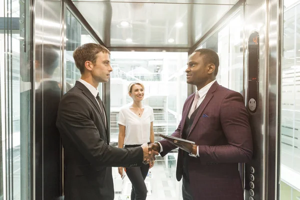 Hombres de negocios jóvenes y exitosos en el centro de negocios de ascensores cabalga al trabajo. apretón de manos — Foto de Stock