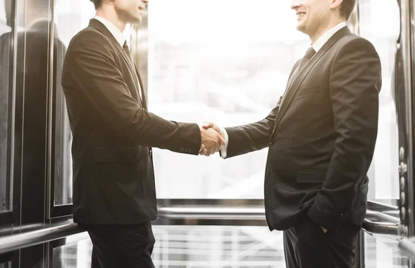 successful and young businessmen in the elevator business center rides to work. business handshake