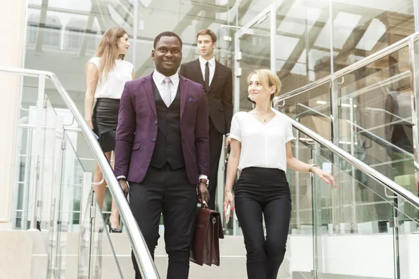 Jóvenes empresarios bajan las escaleras y se comunican. Hombre afroamericano y mujer europea — Foto de Stock