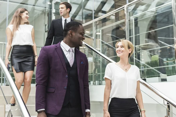 Jóvenes empresarios bajan las escaleras y se comunican. Hombre afroamericano y mujer europea — Foto de Stock