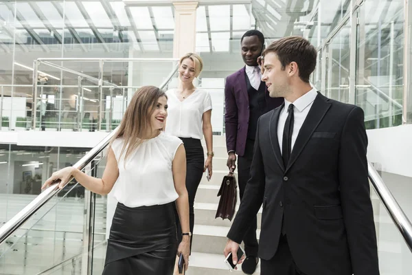 Jóvenes empresarios bajan las escaleras y se comunican. Hombre afroamericano y mujer europea — Foto de Stock