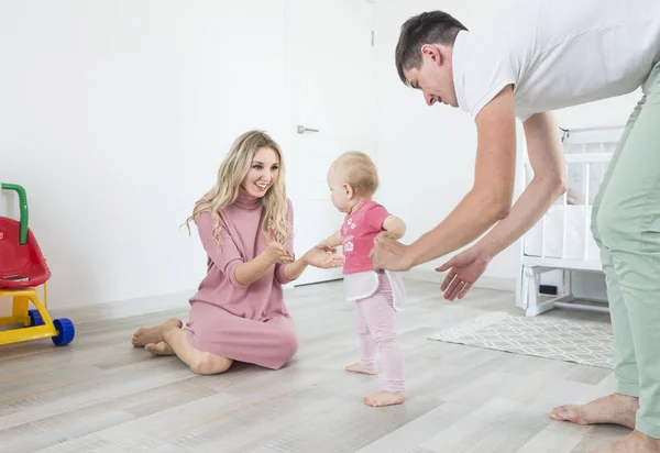 Smiling happy young mother and father standing in their living room at home affectionately cradling the cute baby girl in their arms. the child learns to walk, the first steps — Stock Photo, Image