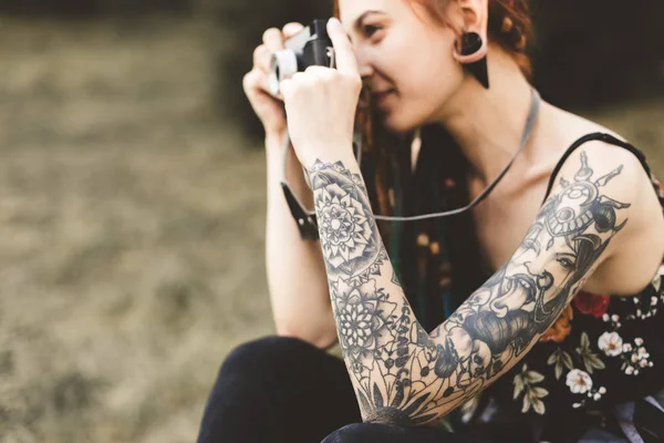 Chica joven con tatuajes y rastas fotografías cámara vintage en el parque — Foto de Stock