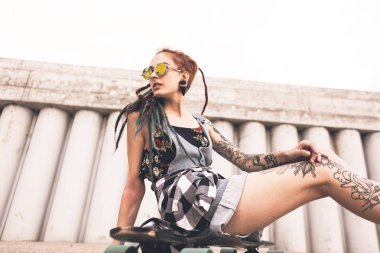 dövme ve dreadlocks bir longboard beton yapı zemin üzerine oturan genç kız