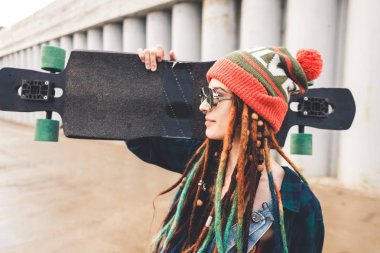 Güneş gözlüklü genç kız ve bir kap duruyor bir longboard beton yapı arka planı ile
