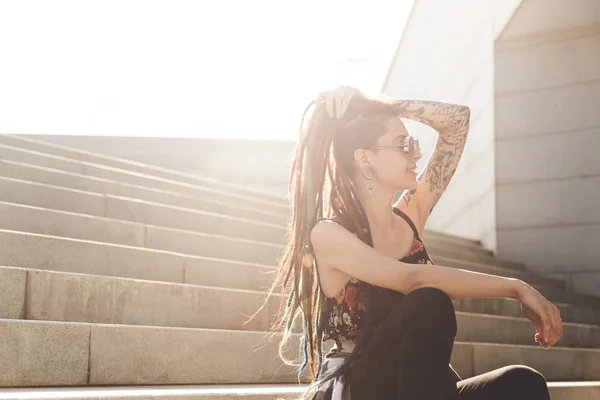 Chica joven con tatuaje y rastas sentado en las escaleras —  Fotos de Stock