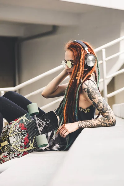 UFA, RUSIA - 12 de septiembre de 2018 Foto editorial de una joven con tatuaje y rastas escuchando música mientras está sentada en las escaleras —  Fotos de Stock