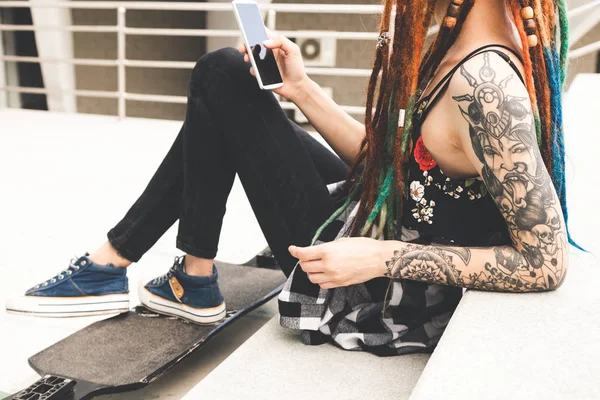 Chica joven con tatuaje y rastas escuchando música mientras se sienta en los escalones —  Fotos de Stock