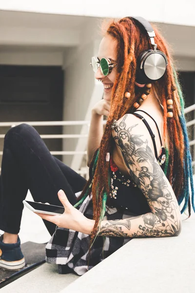 Νεαρό κορίτσι με τατουάζ και dreadlocks ακούτε μουσική ενώ κάθεται στα σκαλιά — Φωτογραφία Αρχείου
