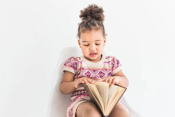 Retrato de una niña con un vestido colorido leyendo un libro sobre un fondo blanco — Foto de Stock