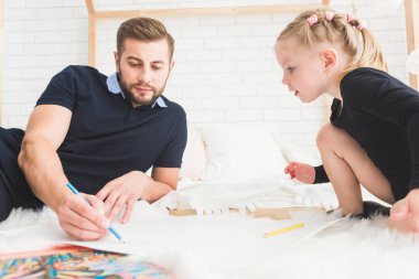 Genç bir baba ve kızı yere yat ve renkli kalemler ile çizmek.