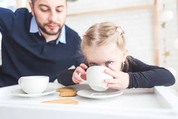 Linda niña y su padre beben té con galletas en casa . — Foto de Stock