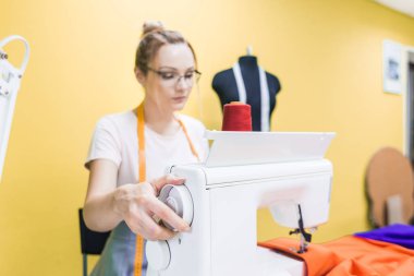 Dikiş atölyesi. Terzi iş başında. Dikiş makinesi ile renkli bir arka plan üzerine çalışan genç kadın