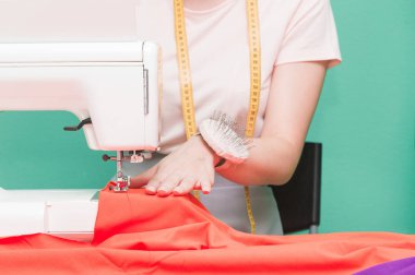 Dikiş atölyesi. Terzi iş başında. Dikiş makinesi ile renkli bir arka plan üzerine çalışan genç kadın