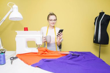 Dikiş atölyesi. Terzi iş başında. Dikiş makinesi ile renkli bir arka plan üzerine çalışan genç kadın