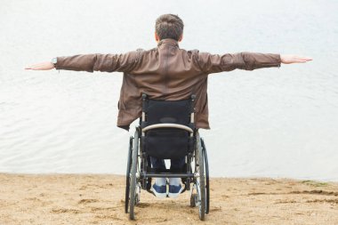 Göl kenarında bir tekerlekli sandalyede oturan genç adam.