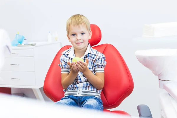 Dental clinic. Reception, examination of the patient. Teeth care. Little boy holding an apple while sitting in a dental chair