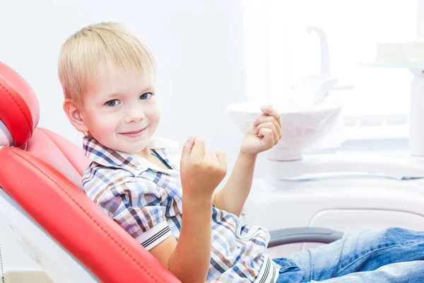 Dental clinic. Reception, examination of the patient. Teeth care. A little boy with dental floss sits in a dental chair. Oral hygiene concept.
