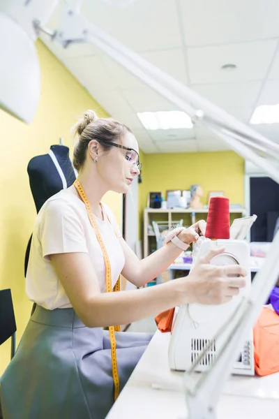 Швейна майстерня. Швачка на роботі. Молода жінка працює з швейною машиною на кольоровому фоні — стокове фото