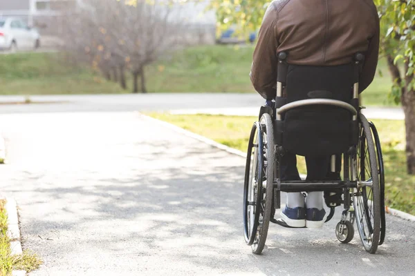 Ein junger Mann im Rollstuhl fährt die Parkstraße entlang. — Stockfoto