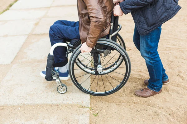 Νεαρός άνδρας σε αναπηρικό καρότσι με τον Βοηθό του σε μια βόλτα στο πάρκο. — Φωτογραφία Αρχείου