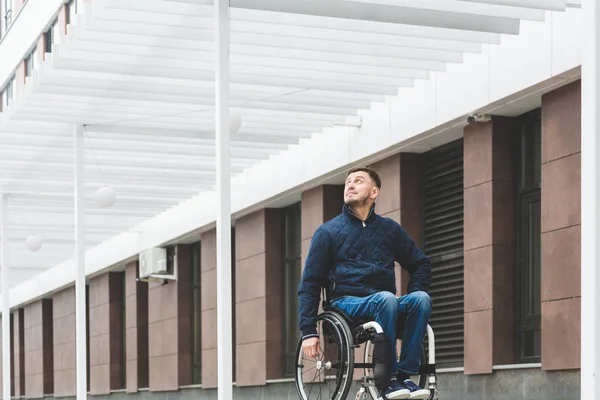 Young man in a wheelchair against the backdrop of a modern high-rise building. — Stock Photo, Image