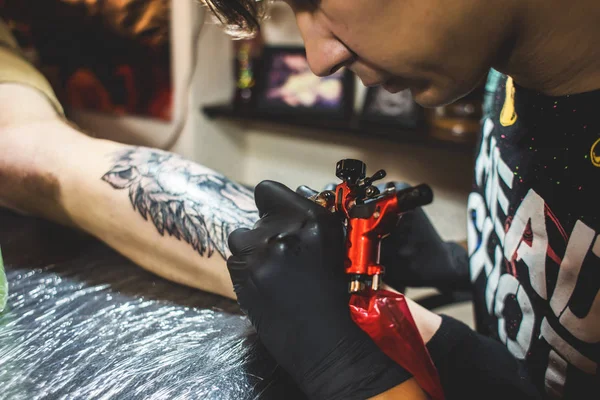 The tattoo artist creates a picture on the body of a man. close-up of tattoo machines and hands