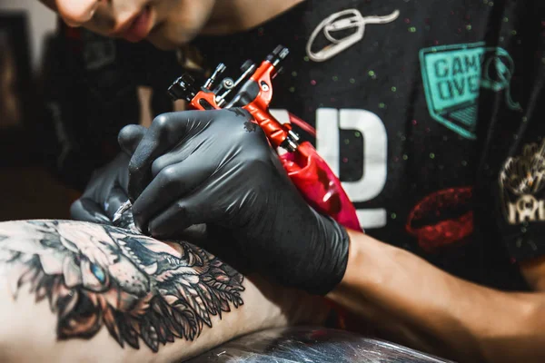 The tattoo artist creates a picture on the body of a man. close-up of tattoo machines and hands