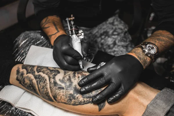 Le tatoueur crée une image sur le corps d'un homme. gros plan des machines à tatouer et des mains — Photo